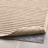 Tapis clair avec rayures foncées et support en feutre pour une adhérence antidérapante au sol.
