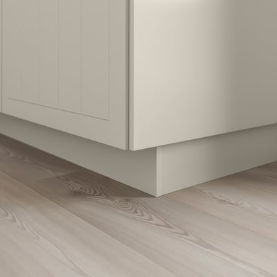 Socle d’armoire de cuisine blanc sur plancher en bois clair, cachant l’espace, donnant un aspect uniforme.