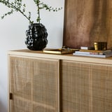 Un vase en grès élégant et texturé sur une armoire en bois, contenant de la verdure fraîche.