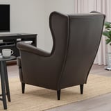 Une chaise à oreilles brun foncé avec un dossier haut et des accoudoirs est posée sur un tapis tissé près d’une table d’appoint avec une tasse.
