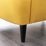 Chaise rembourrée jaune vif avec des pieds noirs robustes sur un plancher en bois.