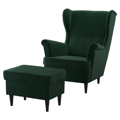 Ensemble chaise à oreilles et pouf en velours vert émeraude. Dos haut, bras roulés, jambes en bois foncé.