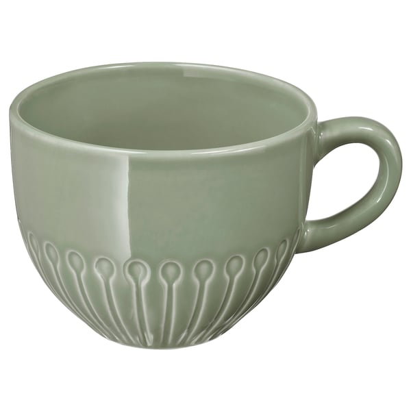 Cette image montre une tasse STRIMMIG verte. Fabriqué en grès, il a un corps lisse avec des motifs de fleurs en relief. Il est rond avec une poignée à droite.
