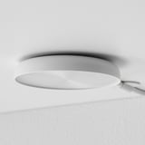 Plafonnier minimaliste moderne, blanc, circulaire, émettant une lueur douce et chaleureuse.