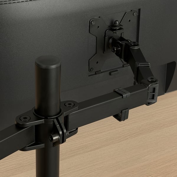 Gros plan du bras de moniteur noir fixé au bureau, montrant des charnières robustes et réglables.