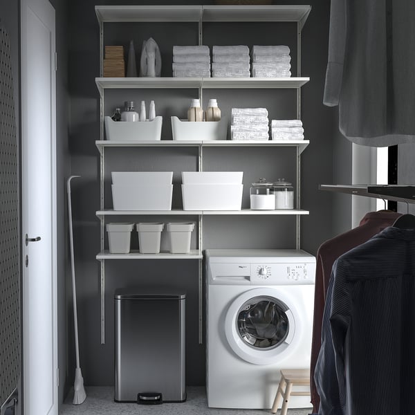 Placard organisé Poubelle à pédale en acier inoxydable SULTEN à côté d’une machine à laver blanche, entourée d’étagères soigneusement rangées avec des articles de linge.