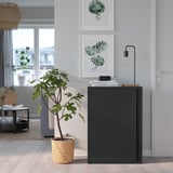 Armoire noire, panier à plantes en osier, impressions d’art, murs gris ; décoration intérieure moderne.