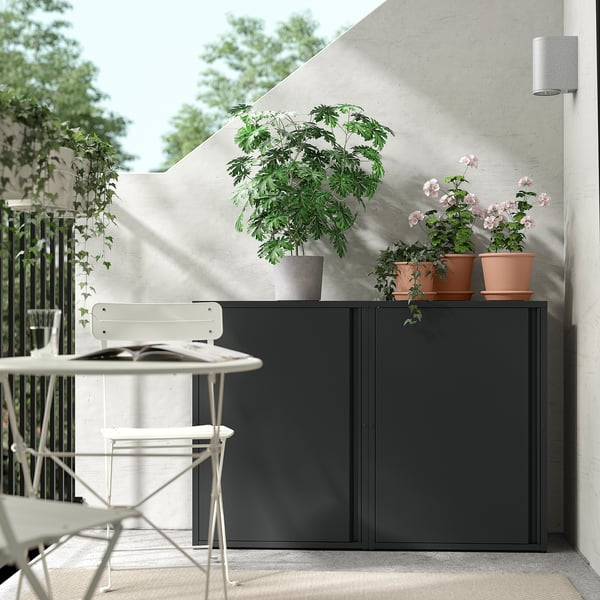 Armoire SUNDSÖ noire avec des plantes sur le dessus, chaises blanches à proximité.