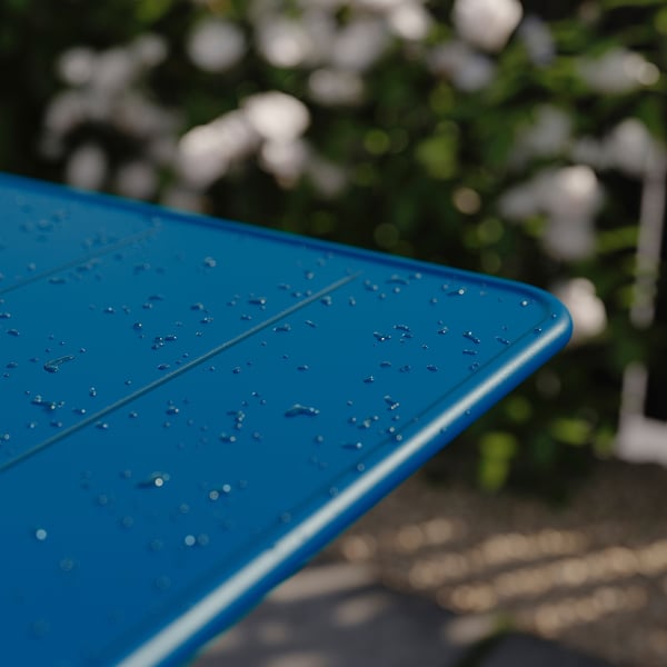 Table d’extérieur bleue avec des gouttelettes d’eau, partiellement pliée, posée contre la verdure.