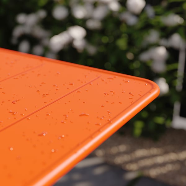 Surface de table pliable orange vif avec gouttelettes d’eau, posée à l’extérieur.