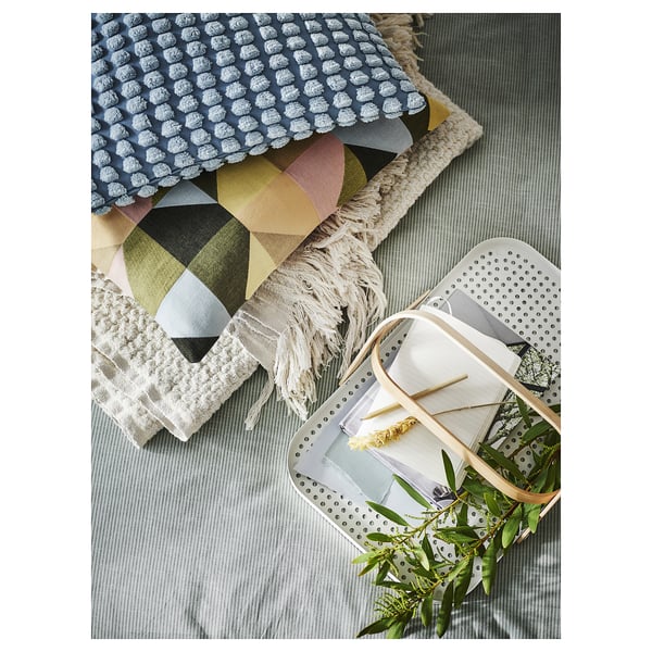 Coussins géométriques colorés sur fond gris avec plateau à pois blancs et verdure.