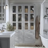Armoire TÄNNFORSEN grise avec portes et tiroirs en verre dans la salle de bains à côté de la baignoire et du lavabo.
