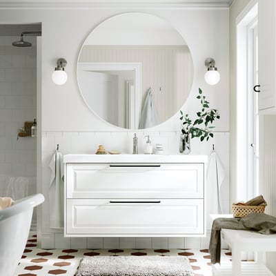 Salle de bains élégante avec meuble-lavabo TÄNNFORSEN, miroir et tiroirs. Carrelage blanc, sol à motifs, plantes vertes. Mélange moderne et classique.