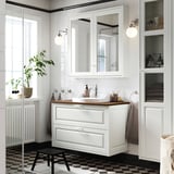 Vanité de salle de bain blanche moderne avec comptoir en bois, armoire à miroir au-dessus et carreaux de sol noirs.