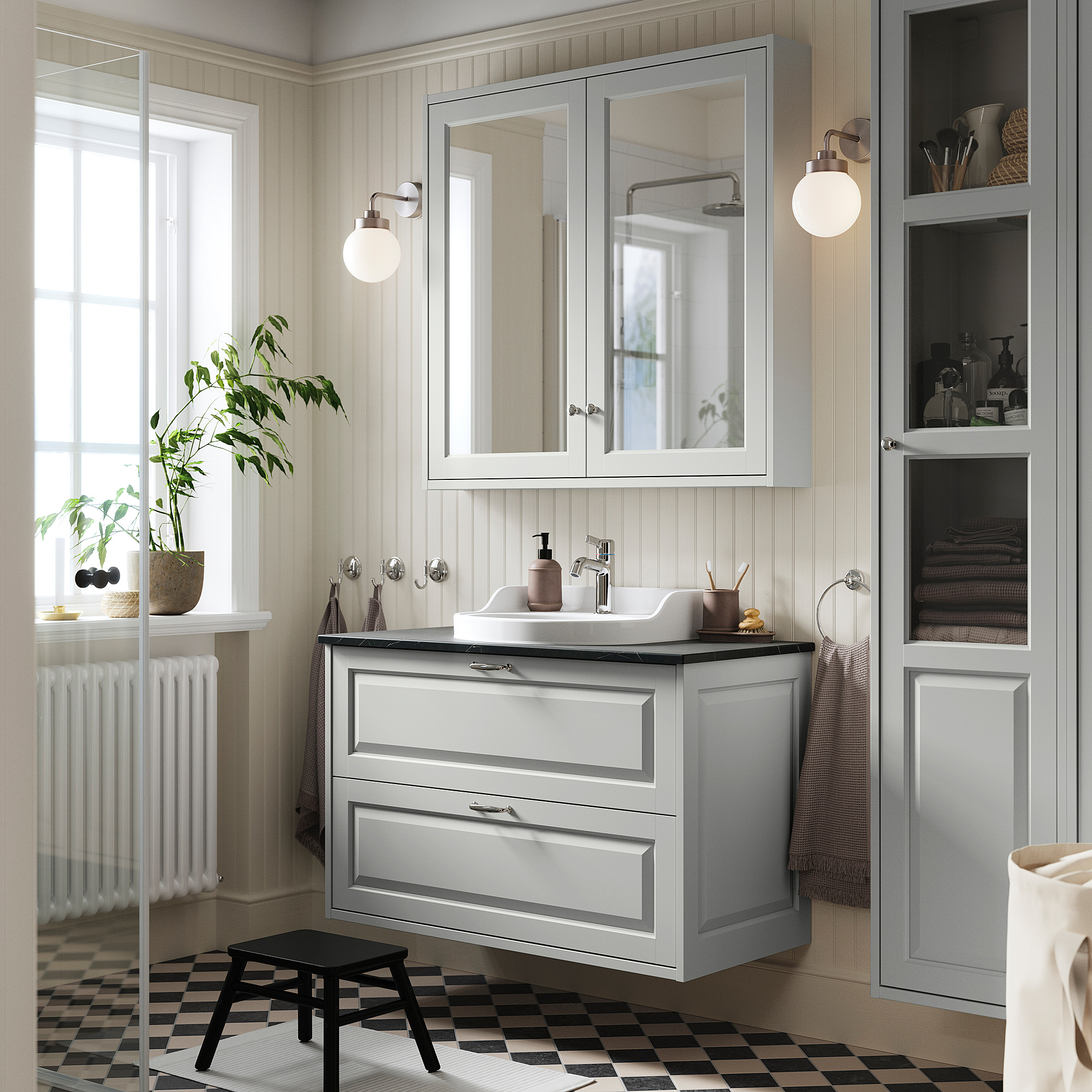 Salle de bain grise moderne avec meuble-lavabo TÄNNFORSEN, grand miroir et lavabo élégant. Des plantes et des serviettes décorent l’espace.