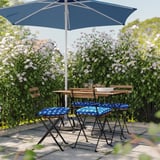Configuration du patio avec des chaises rembourrées à pois bleus et blancs, une table en bois et un parasol bleu marine sous des fleurs blanches épanouies.