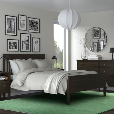 Chambre avec des meubles en bois sombre, un grand lit blanc, des photos encadrées, un miroir rond, une lampe suspendue et un tapis vert. Le tapis a une taille : grande.