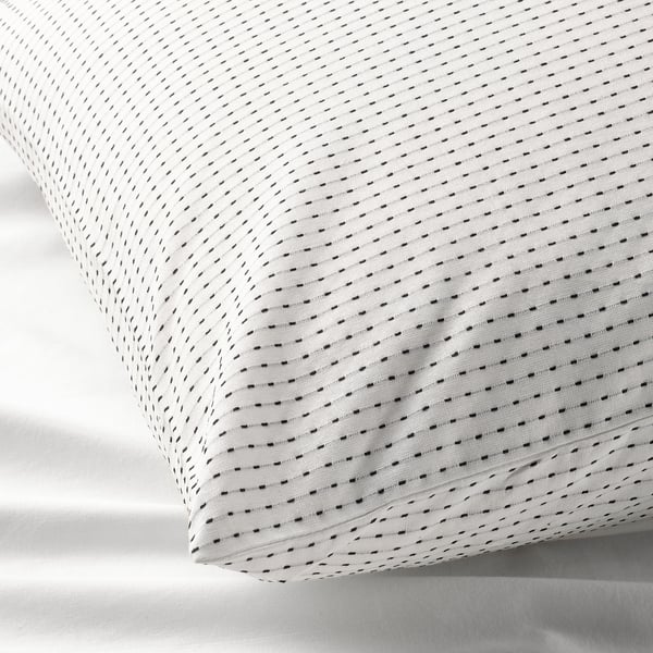 Gros plan de l’élégante taie d’oreiller TÅGVECKLARE blanche avec un motif cousu complexe, mettant en valeur la texture et le savoir-faire du coton de haute qualité.