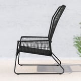 Chaise d’extérieur en osier noir avec dossier et assise incurvés, adossée à un mur clair. Design minimaliste, confortable pour se détendre.