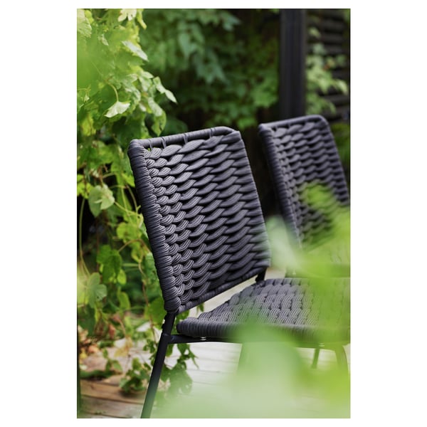 Chaises d’extérieur en osier noir, empilées, avec des plantes vertes en arrière-plan.