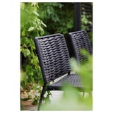 Chaises d’extérieur en osier noir, empilées, avec des plantes vertes en arrière-plan.