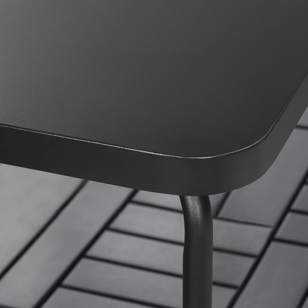Table d’extérieur noire avec des pieds en métal élégants sur un plancher en bois.