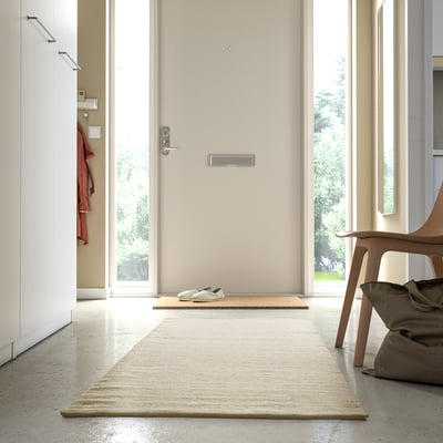 Couloir minimaliste avec tapis beige central, légèrement plus grand que le paillasson, doux et accueillant.