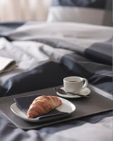 Un plateau TILLGÅNG en plastique polypropylène noir contenant une pâtisserie et une tasse à café sur un lit.