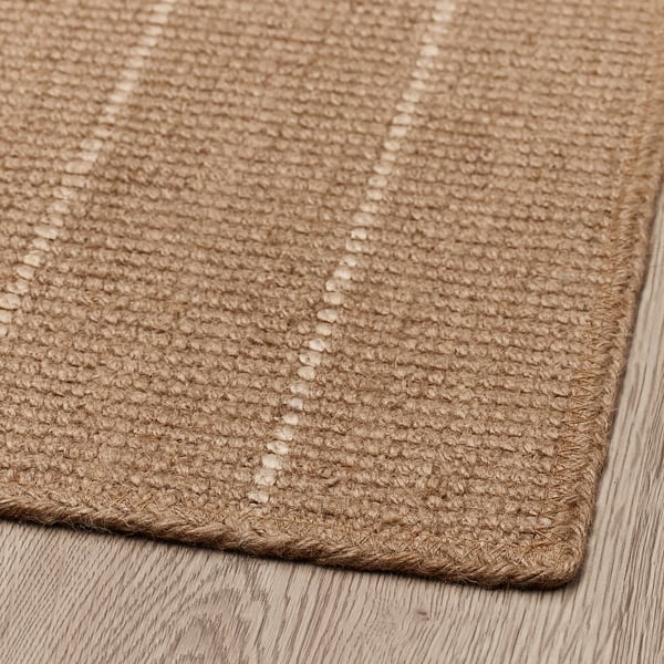 Paillasson en jute aux bords tressés, soigneusement posé sur un plancher en bois, mettant en valeur un tissage complexe et une texture naturelle.