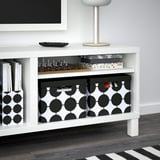 Meuble TV blanc avec étagères de rangement. Comprend des boîtes à motifs noirs et blancs, contenant des jeux comme les échecs et le bingo, des livres et d’autres articles.