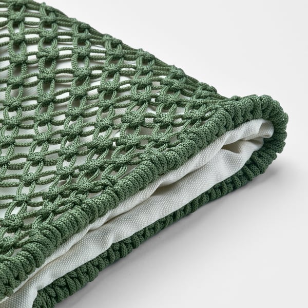 Housse de coussin en crochet vert montrée, pliée soigneusement, affichant un motif complexe et une doublure intérieure blanche.