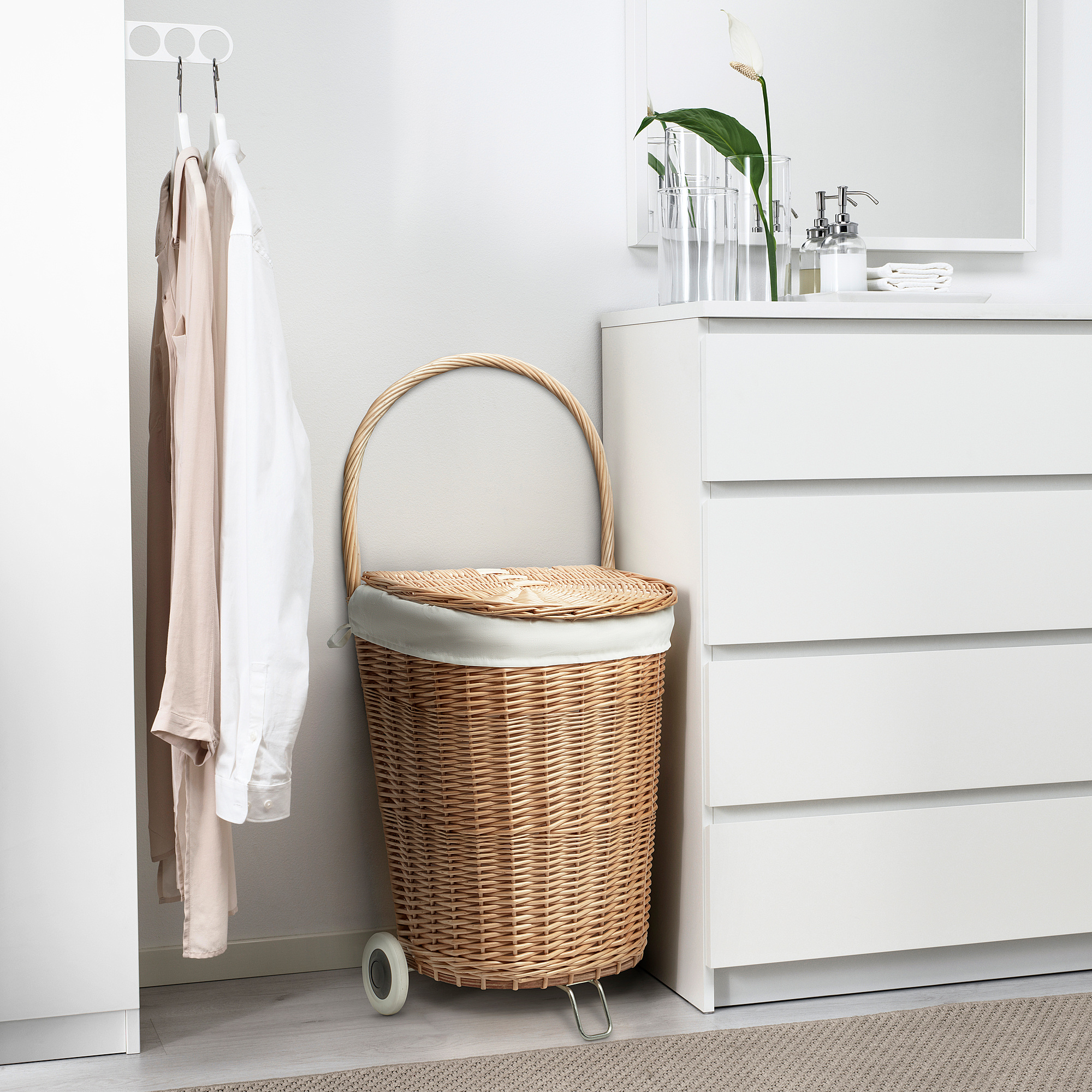 Panier à linge tissé à la main avec roues, poignée, à côté de l’armoire et du cintre. Taille moyenne.