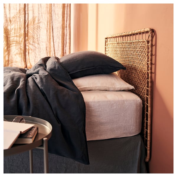Lit avec tête de lit en osier, draps gris, cadre confortable de la chambre.