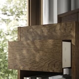 Meuble à tiroirs en bois foncé au design moderne et aux tiroirs à fermeture douce, positionné près d’une fenêtre avec vue extérieure verdoyante.