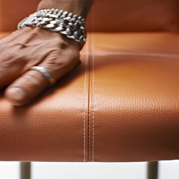 Gros plan d’une chaise rembourrée élégante et de haute qualité avec des coutures apparentes et d’une main d’une personne portant un bracelet posé dessus.