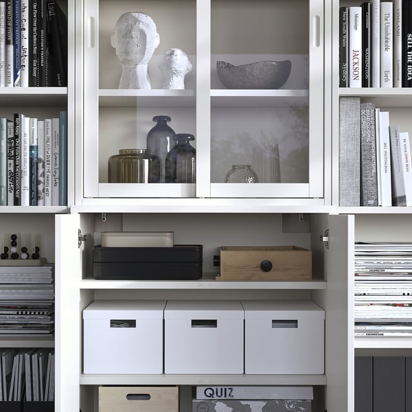 Étagère avec portes vitrées : blanc, divers livres, vases et sculptures soigneusement exposés.