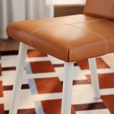 Tabouret marron, pieds blancs, coutures, tapis à motifs.