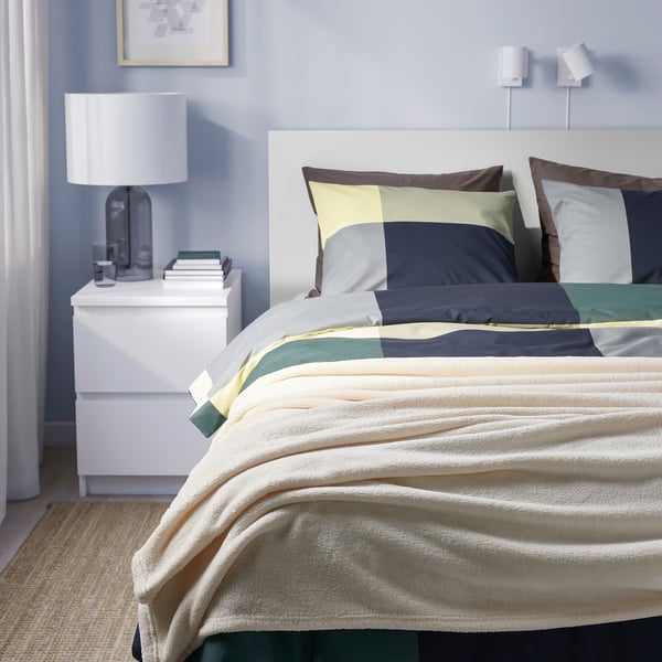 Chambre moderne avec couvre-lit rayé sur grand lit, tête de lit blanche, polyester recyclé, coussins divers.