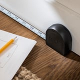 Un mètre ruban TRIXIG noir avec un crayon jaune sur une table en bois, mettant en valeur sa fonction de retour automatique et son mécanisme de verrouillage.