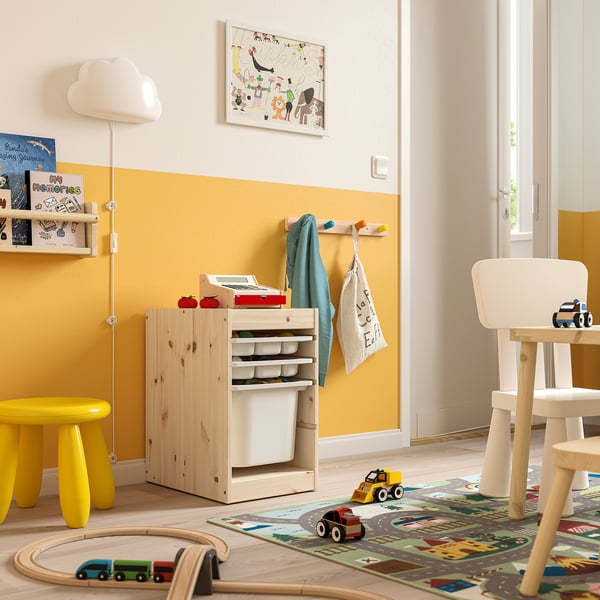 Salle de jeux lumineuse pour enfants avec rangement TROFAST en bois naturel et blanc. Des boîtes en filet et en plastique, un tabouret jaune et des jouets en bois.
