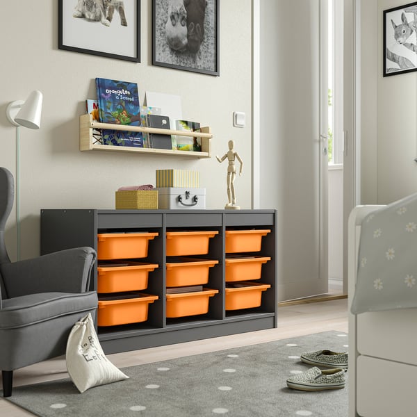 Rangement TROFAST dans la chambre avec boîtes orange, chaise grise, porte blanche, étagère et lampe.