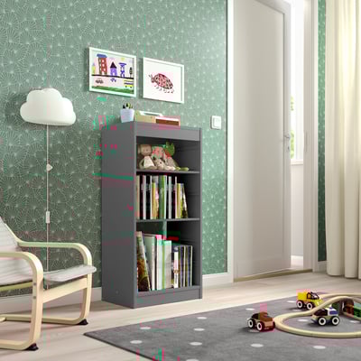 Étagère TROFAST grise dans la chambre d’enfant avec jouets et livres. Près de la chaise et de la porte fermée.