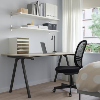 Bureau TROTTEN beige avec pieds noirs, sous étagères blanches, chaise noire, fenêtre, plante.