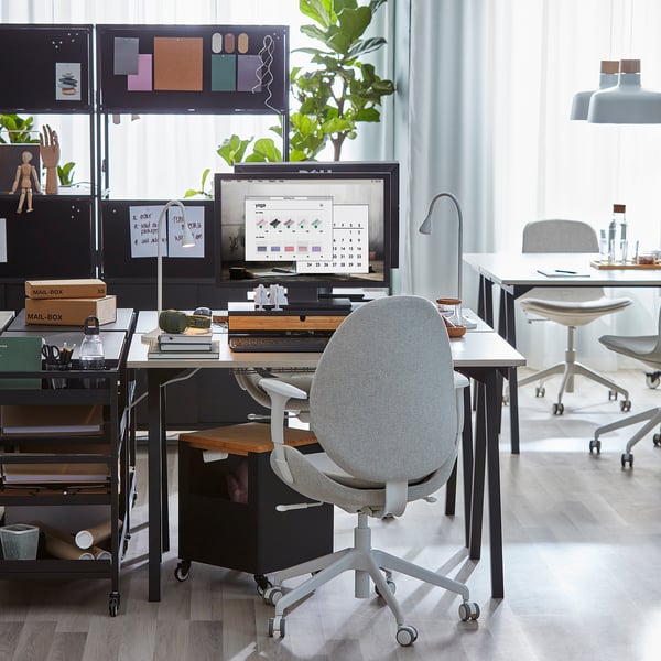 Espace de travail moderne avec bureau TROTTEN, pieds uniques, moniteur et chaise. La pièce est bien éclairée avec une fenêtre et une lumière suspendue.