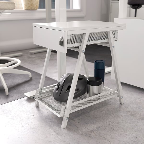 Une unité de rangement TROTTEN blanche avec un tiroir verrouillable et une étagère inférieure contenant des objets comme un casque, des tasses et une souris.