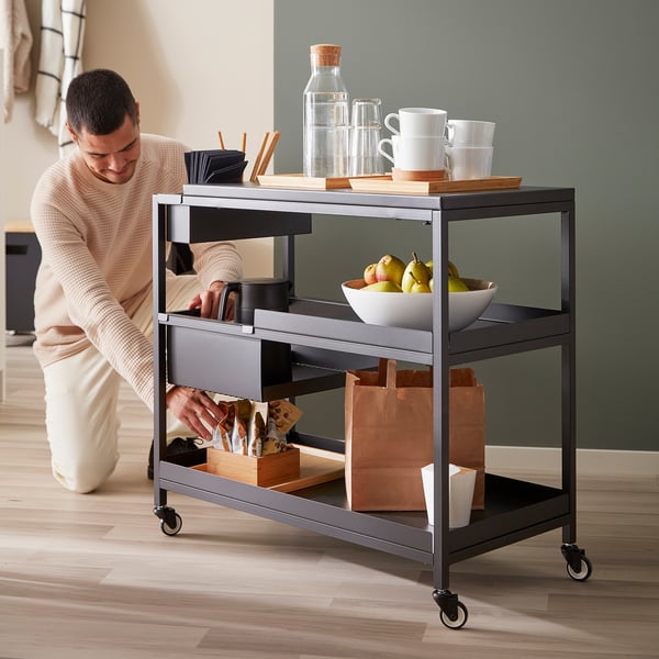 Homme organisant un chariot de bureau avec des tasses, des fruits, une cruche, un sac et des fournitures.