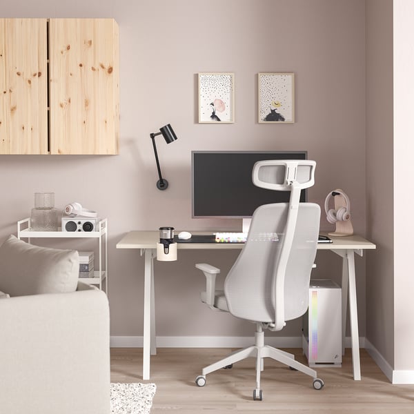 Bureau à domicile moderne : bureau en bois clair, chaise TROTTEN blanche, murs roses. Lampe intégrée, moniteur, haut-parleurs, écouteurs et art abstrait.