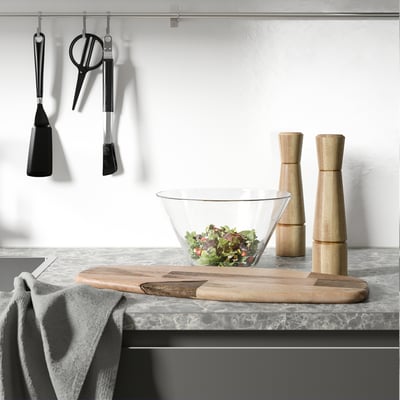 Comptoir de cuisine avec saladier, moulins à poivre et à sel, outils suspendus et une serviette.