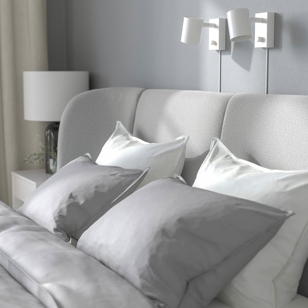 Lit confortable avec tête de lit incurvée, oreillers moelleux et table de chevet avec lampe.