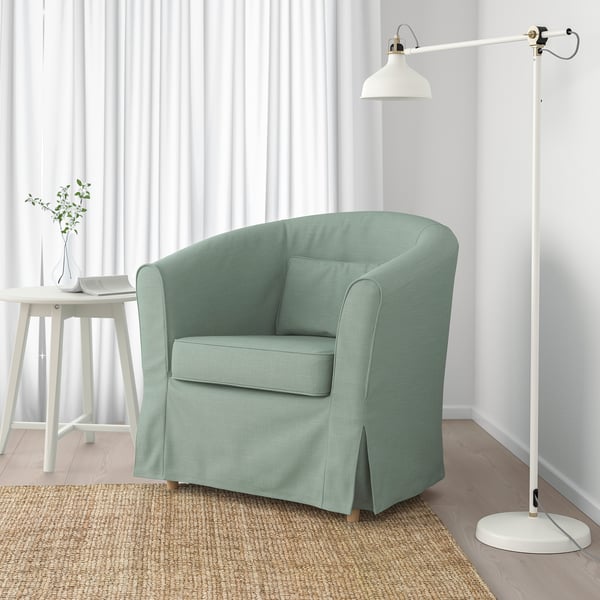 Fauteuil vert avec coussin et lampe sur tapis de jute. Ou, pour rester dans la limite de 150 caractères : fauteuil vert avec coussin et lampe sur tapis.